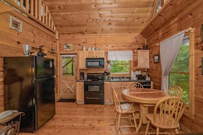 Una baita in legno con cucina, dotata di frigorifero, fornello, microonde e pensili in legno.