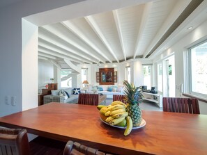 A dining area with a wooden table, a bowl of fruit, and a view of the living room.