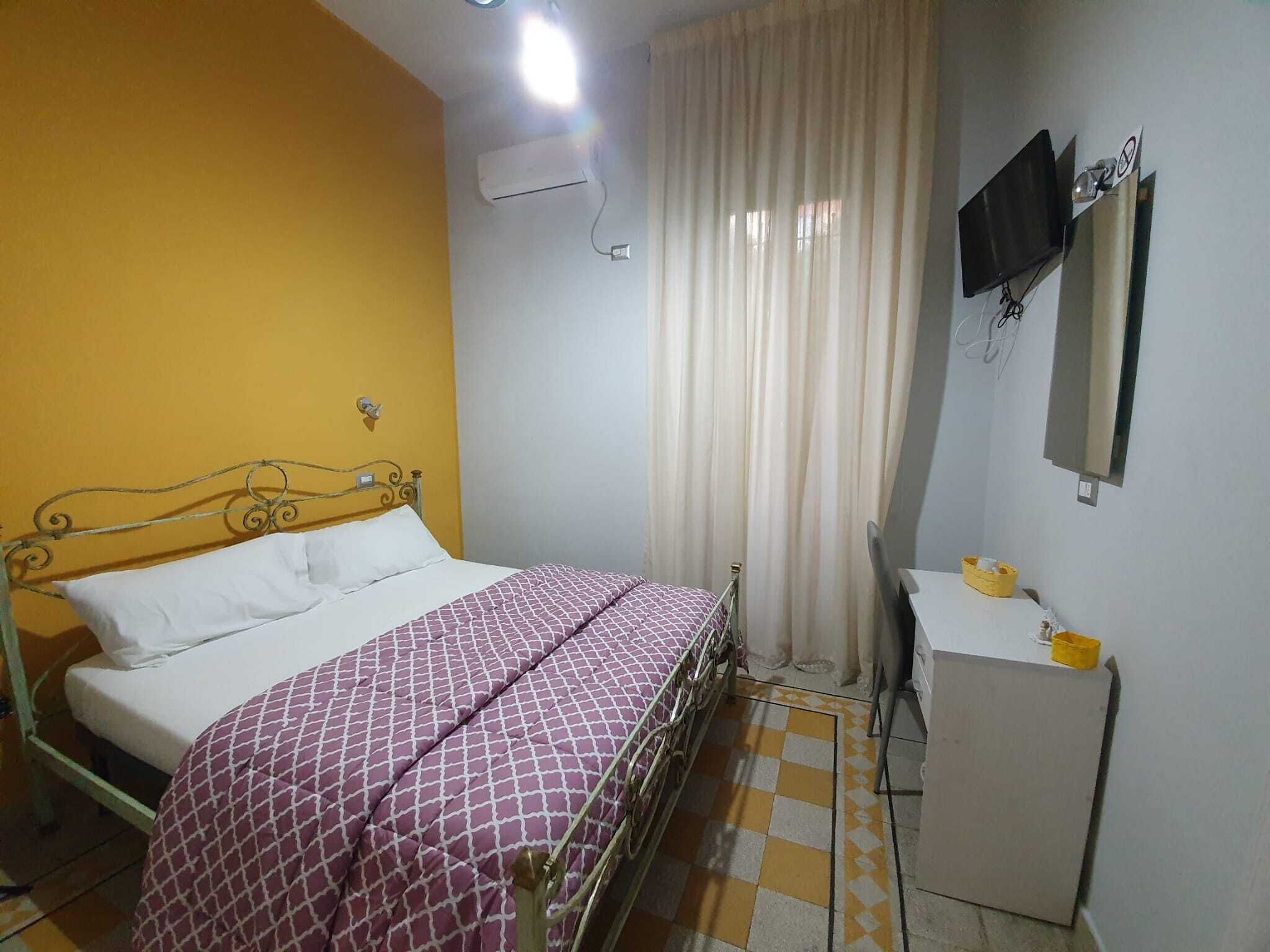 A bedroom with a bed, a desk, a chair, a mirror, and an air conditioning unit.