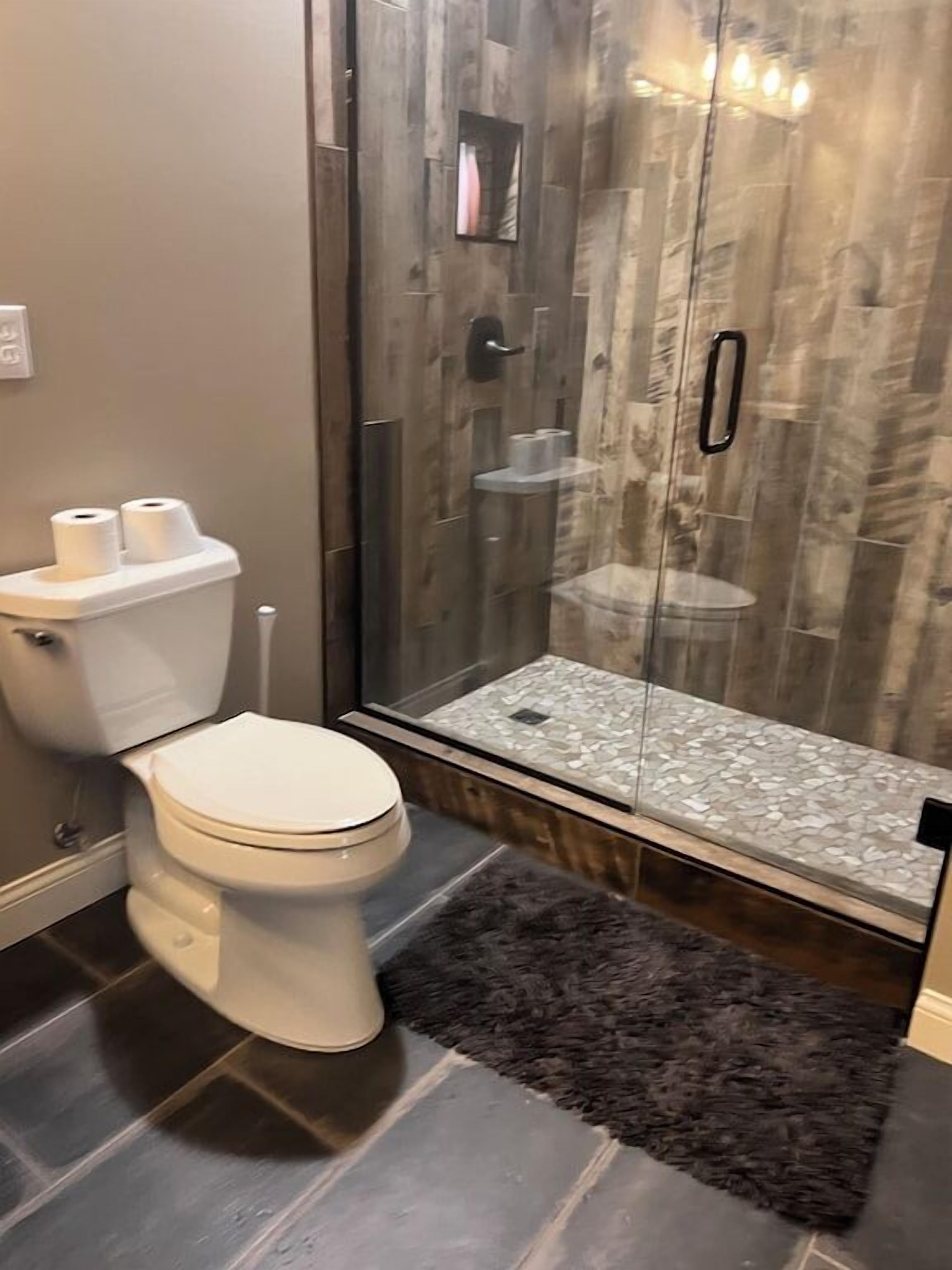 A modern bathroom with a toilet, a glass shower enclosure, and a textured shower floor.