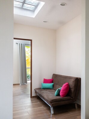 A modern living room with a brown sofa, teal and pink cushions, and a skylight above. - Beautiful, comfortable two bedroom home with pool (Puerto Morelos)