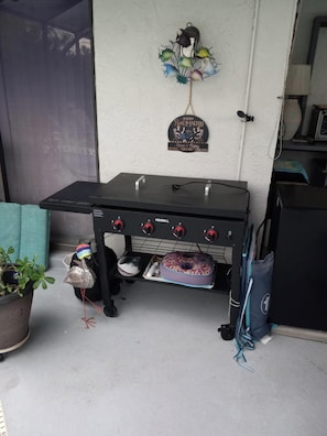 A barbecue grill with four burners, a decorative sign above it, a potted plant, and a bag on the floor. - Rager's BnB Suite (Port Charlotte)