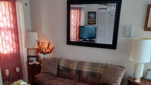 Een woonkamer met een bruine bank, een houten salontafel, een paarse fauteuil en een aan de muur bevestigde televisie.