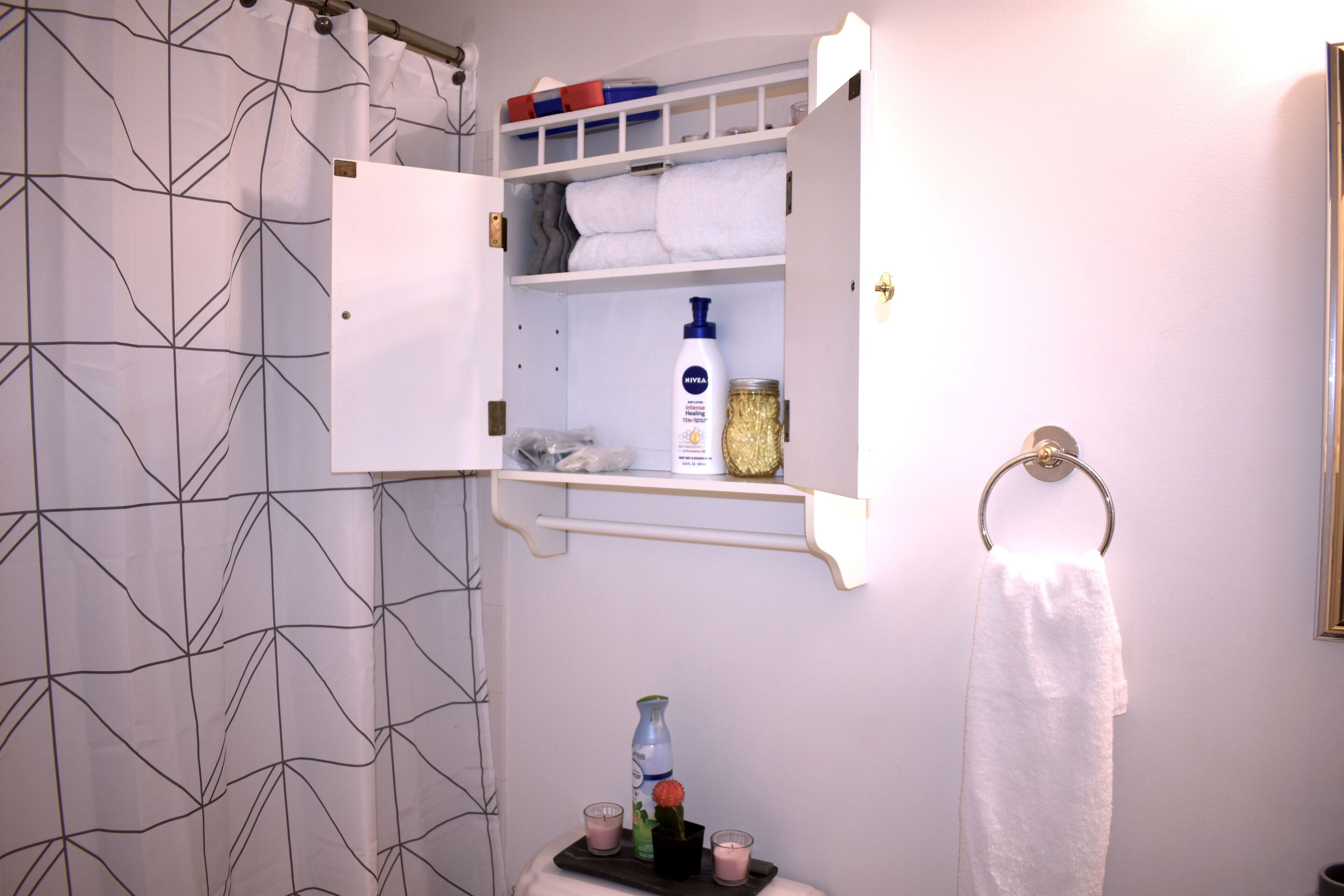 A bathroom with a shower curtain, a towel rack, a shelf with toiletries, and a small table with candles.