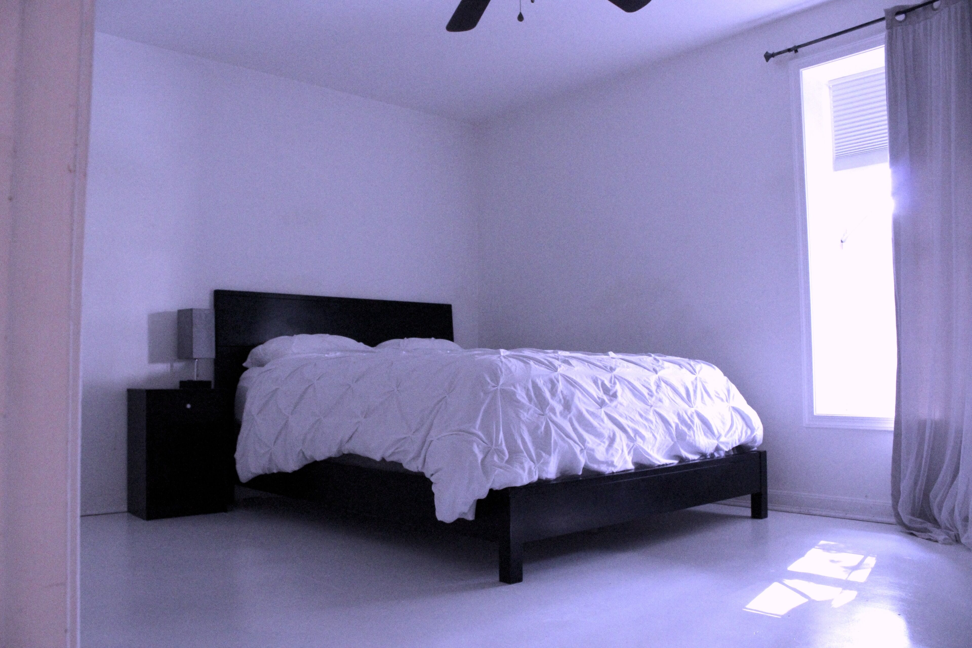 Una camera da letto con un letto, un comodino e una finestra con tende.