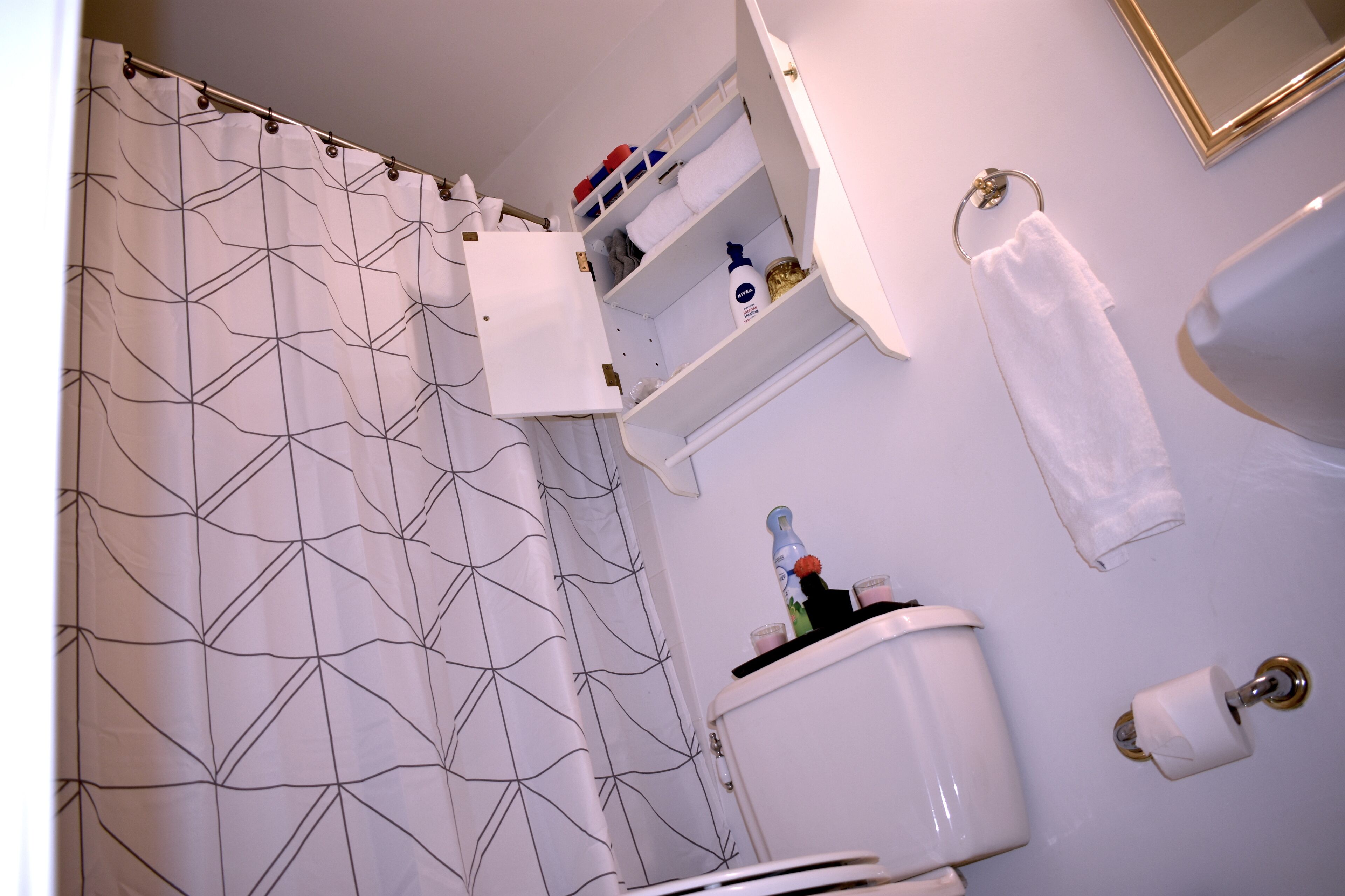 Une salle de bain avec un rideau de douche à motifs géométriques, des toilettes, une étagère avec des articles de toilette et un porte-serviettes.