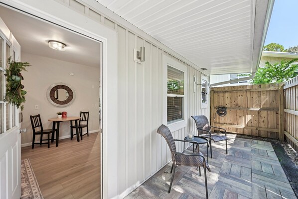 A covered patio with a wooden deck, a dining area with a table and chairs, and a wooden fence.