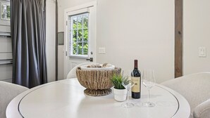 A round table with a woven bowl, a potted plant, a wine bottle, and two wine glasses. - Pet Friendly Studio with Private Fenced Yard (Jacksonville)