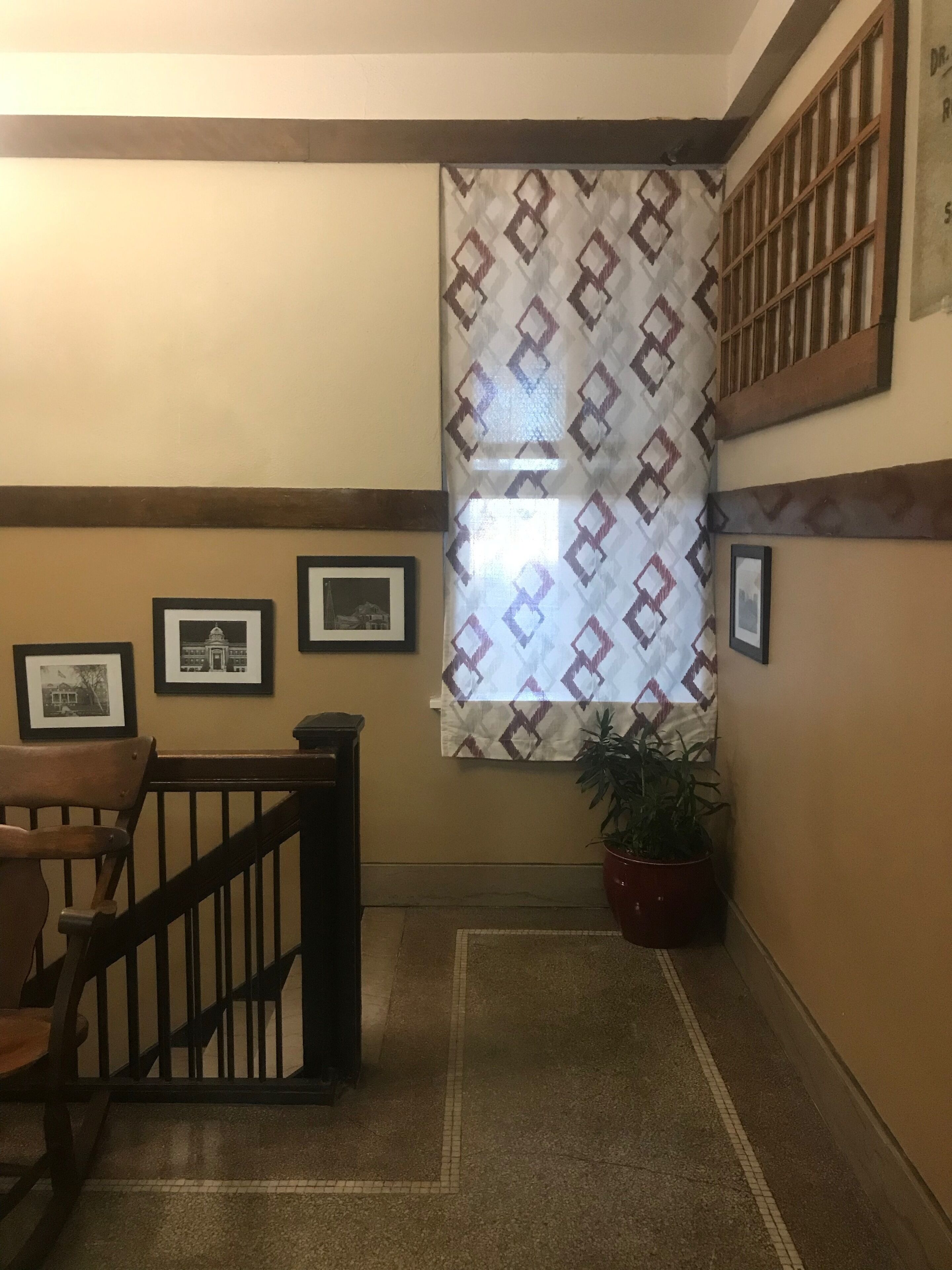 A staircase with a wooden railing, a patterned window, and framed pictures on the wall.
