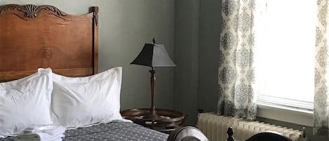 A bedroom with a wooden bed, a bedside table with a lamp, a chair, and a window with patterned curtains.