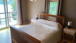 Ein Schlafzimmer mit einem Holzkopfteil, einem Bett mit gemustertem Überwurf, zwei Nachttischen mit Lampen und einem Fenster mit Vorhängen.