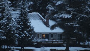 Eine Hütte mit Veranda, umgeben von schneebedeckten Bäumen.