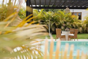 Un'area piscina con tavolo e sedie, circondata da vegetazione lussureggiante e palme.
