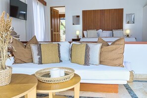 A hotel room with a white sofa, two side tables, a TV, a wooden headboard, and a large window with curtains.
