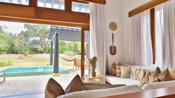 Quarto com sofá, uma mesa pequena e vista para a piscina e jardim.