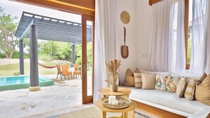 Uma área de estar aconchegante com sofá, uma pequena mesa de madeira e vista para a piscina e o jardim.