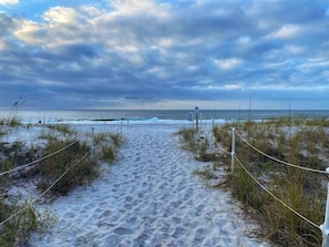 A sandy beach path leading to the ocean with a cloudy sky.