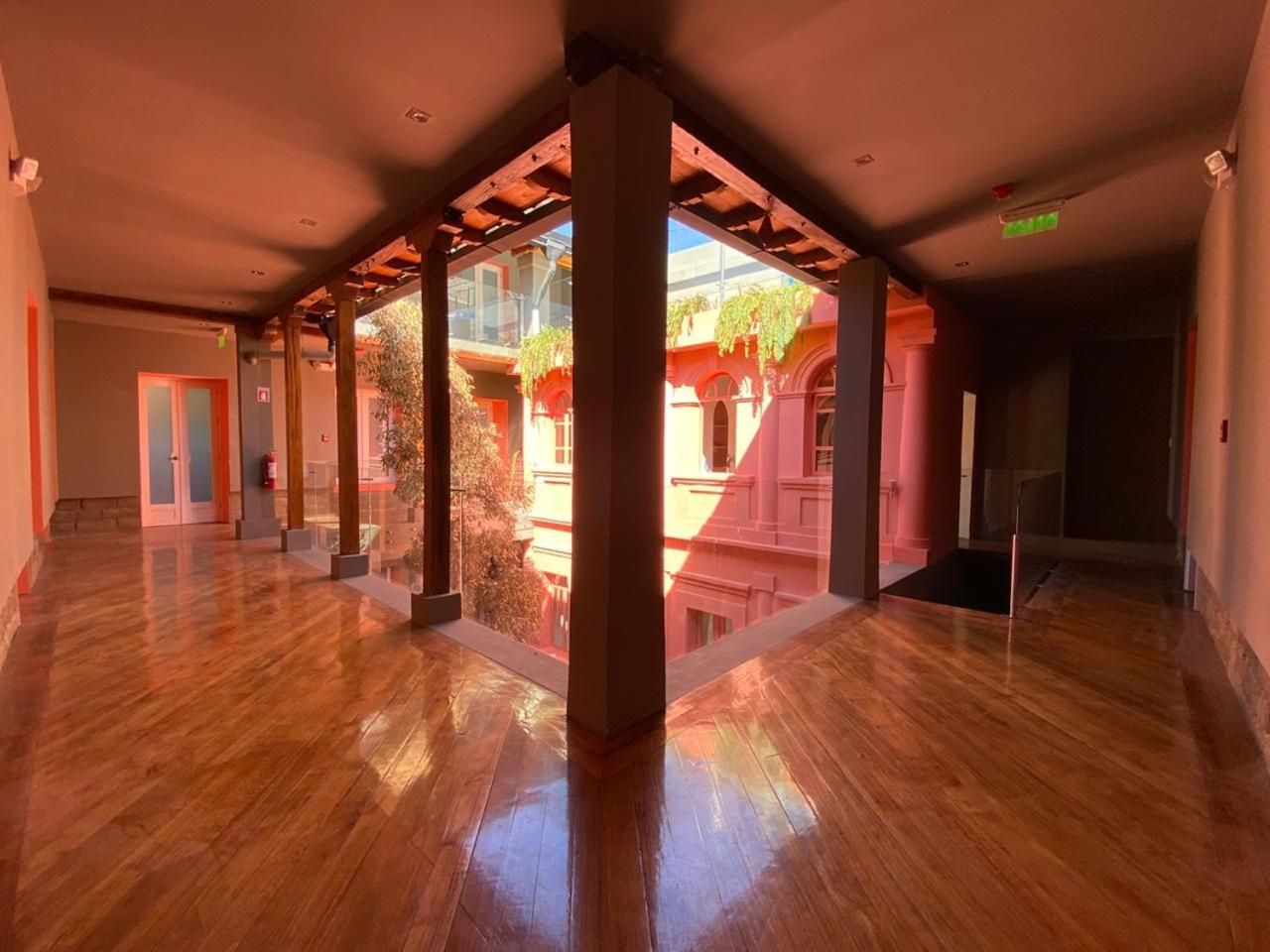 Un vaste couloir doté d’un plancher en bois, de grandes colonnes et de murs en verre offrant une vue sur l’extérieur.