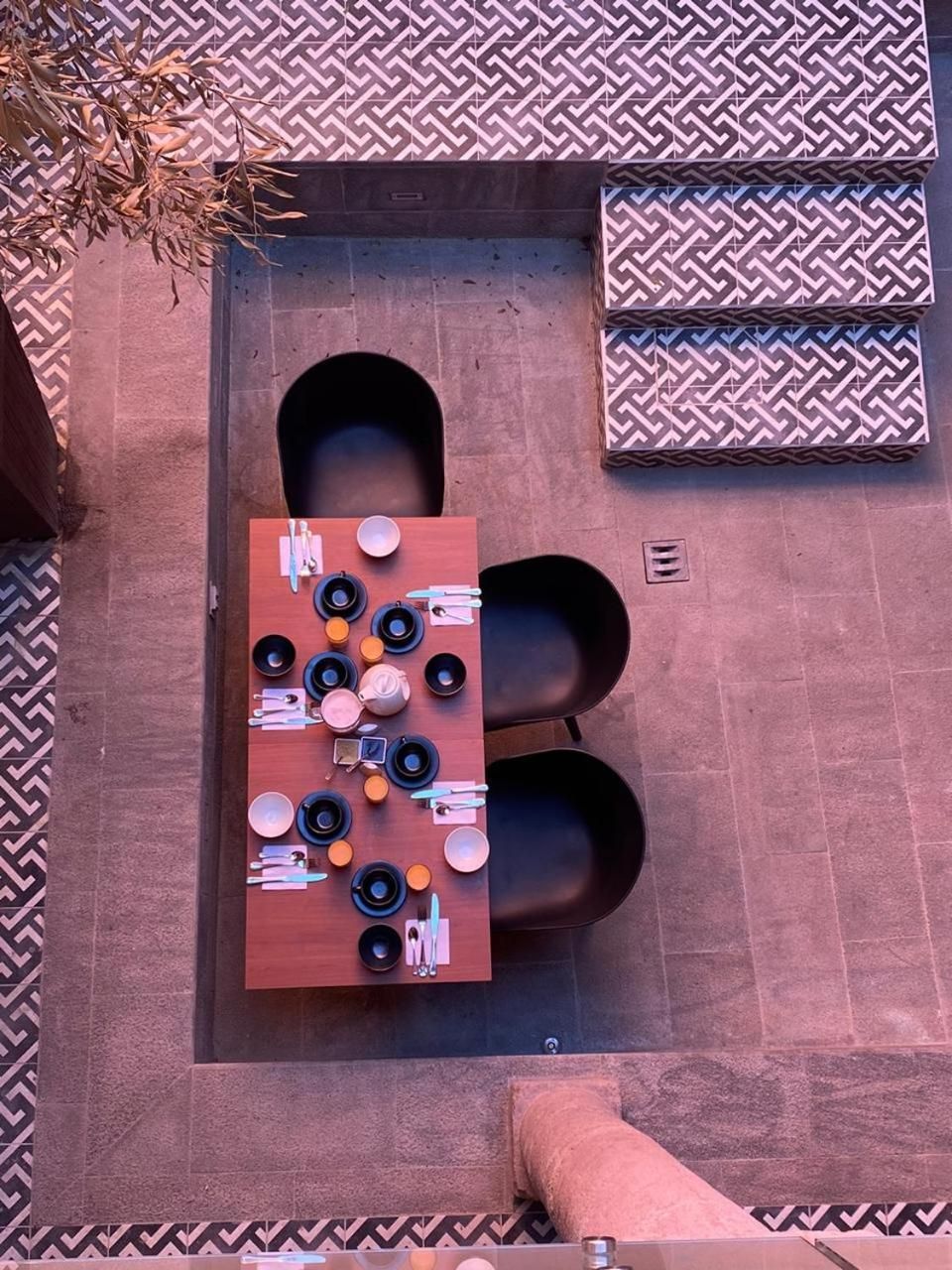 An outdoor dining area with a table set for four, surrounded by chairs, and a patterned wall in the background.
