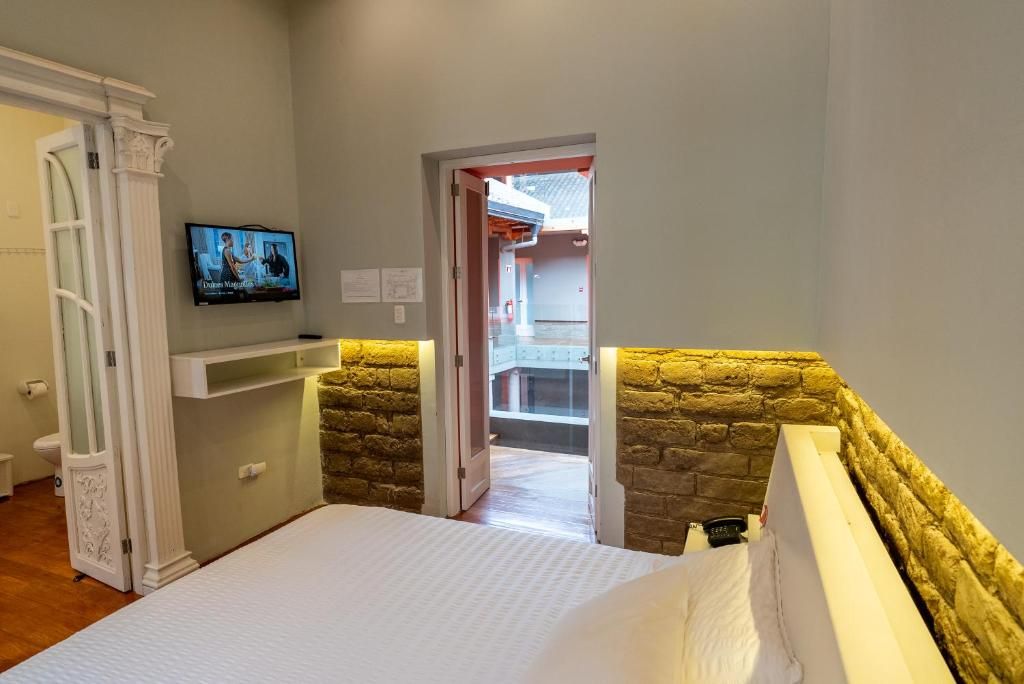 A bedroom with a bed, a television mounted on the wall, and a stone wall.