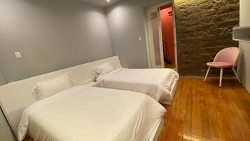 A bedroom with two beds, a stone wall, a wooden floor, and a pink chair.