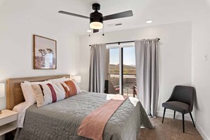 A bedroom with a bed, a chair, a ceiling fan, and a window with curtains. - Desert Lagoon #74 by RedAwning (St. George)