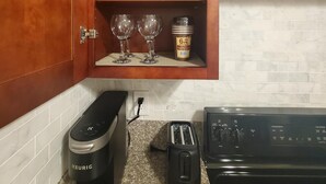 Une cuisine avec un meuble en bois contenant des verres à vin et un pot de glace contenant six portions individuelles. On y trouve également une machine à café Keurig, un grille-pain et une cuisinière.