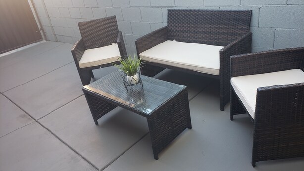 Un espace patio aménagé avec des meubles en osier, comprenant deux chaises et une table, ainsi qu’une plante en pot posée sur la table.