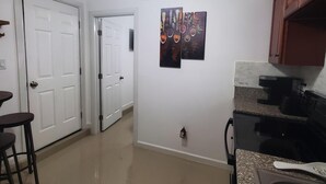 Une cuisine avec un poêle noir, un plan de travail et un ventilateur de plafond. On y trouve deux portes blanches et une petite table avec des tabourets.