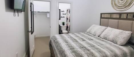 A bedroom with a bed, a ceiling fan, a wall-mounted TV, and a door leading to a bathroom.