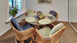 A round glass table surrounded by wicker chairs with cushioned seats, a potted plant, and a decorative item on the table. - Jacksonville Beach Costa Verde 2319-102 by Distinctive Beach Rentals (Jacksonville Beach)