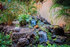 A garden with a small waterfall, lush greenery, and a sign that reads "Rita's Garden". - Maui Vista 1210 by Maui Rental Group (Kihei)