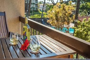 Ein Holztisch mit zwei Gläsern Weißwein und einer Weinflasche auf einem Balkon mit Blick auf einen Pool und Grünflächen.