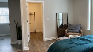 A bedroom with a bed, a chair, a mirror, and a hallway leading to a bathroom. - Newly Built Zen Space 2Bd-3Bth - Pets OK (Lititz)