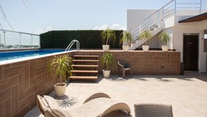 Ein Poolbereich auf dem Dach mit Liegestühlen, Topfpflanzen und einer Treppe zu einer oberen Ebene.