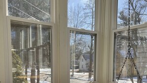 A sunroom with large windows, a swing chair, and a bench with floral cushions. - 3 Bed, 2 Bath Cozy Home Across from Zoo in the heart of Baraboo. (Baraboo)