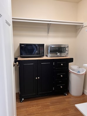 Compact kitchenette with microwave, toaster oven, and trash bin.
