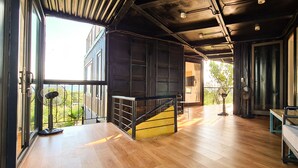 A spacious room with a wooden floor, a staircase, and large windows offering a view of greenery. - Tuan Chau Ruby Villa (Tuan Chau)