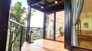 A spacious balcony with a wooden floor, a standing fan, and a view of a garden and building across the street. - Tuan Chau Ruby Villa (Tuan Chau)