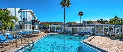 A swimming pool with blue tiles, surrounded by lounge chairs and palm trees.