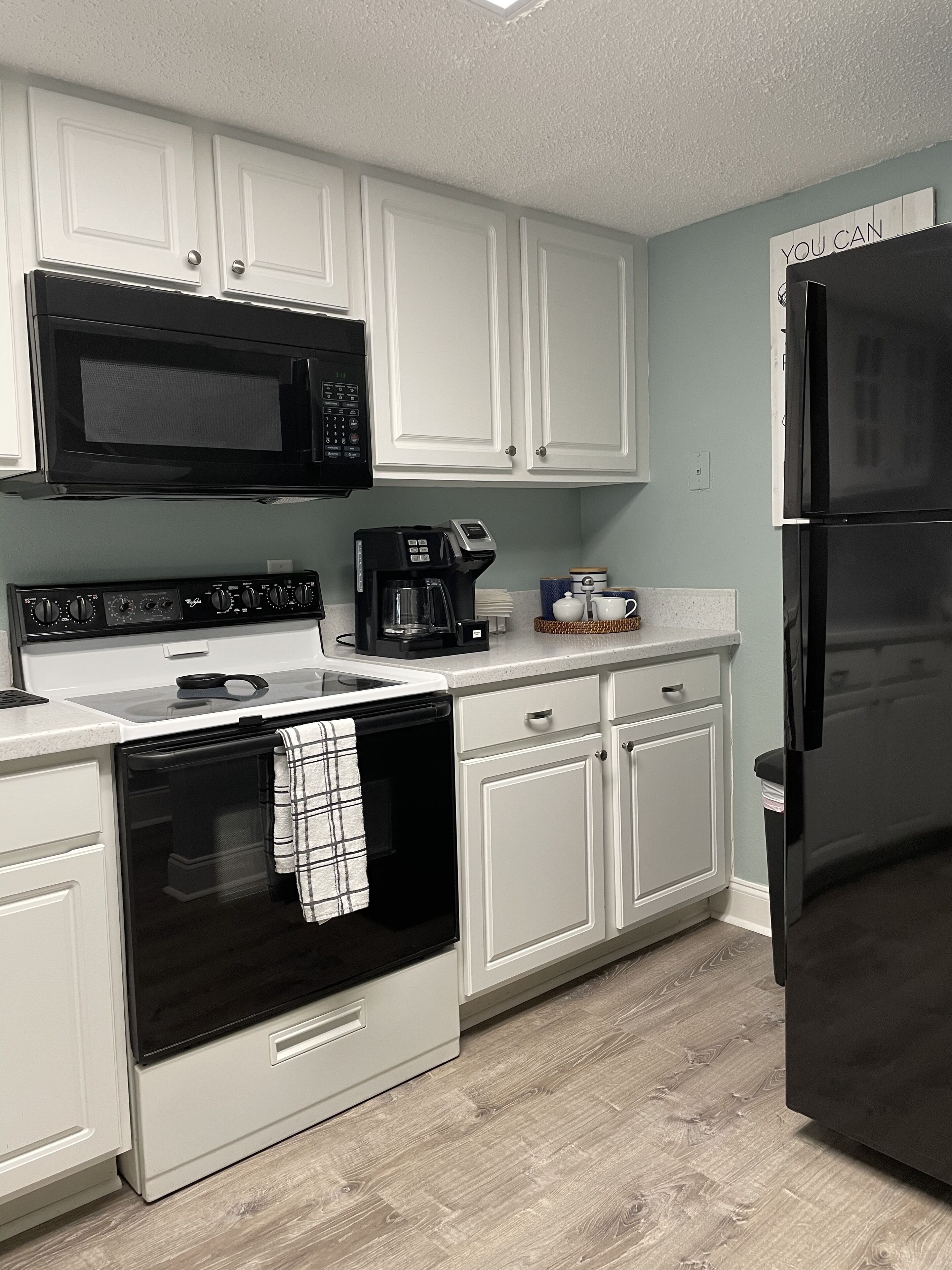 A kitchen with white cabinets, a black microwave, a coffee maker, and a black refrigerator.
