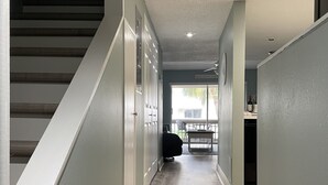 Un pasillo con suelo de madera, paredes blancas y una escalera a la izquierda.