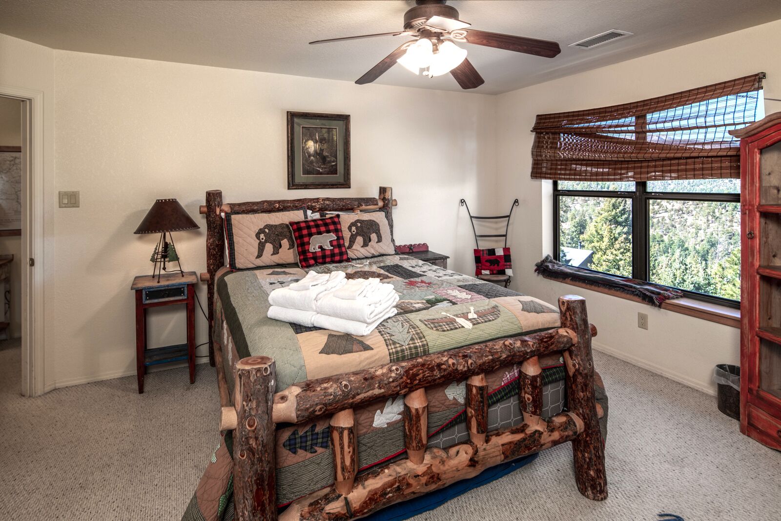 A bedroom with a wooden bed frame, a ceiling fan, a window with blinds, and a framed picture on the wall.