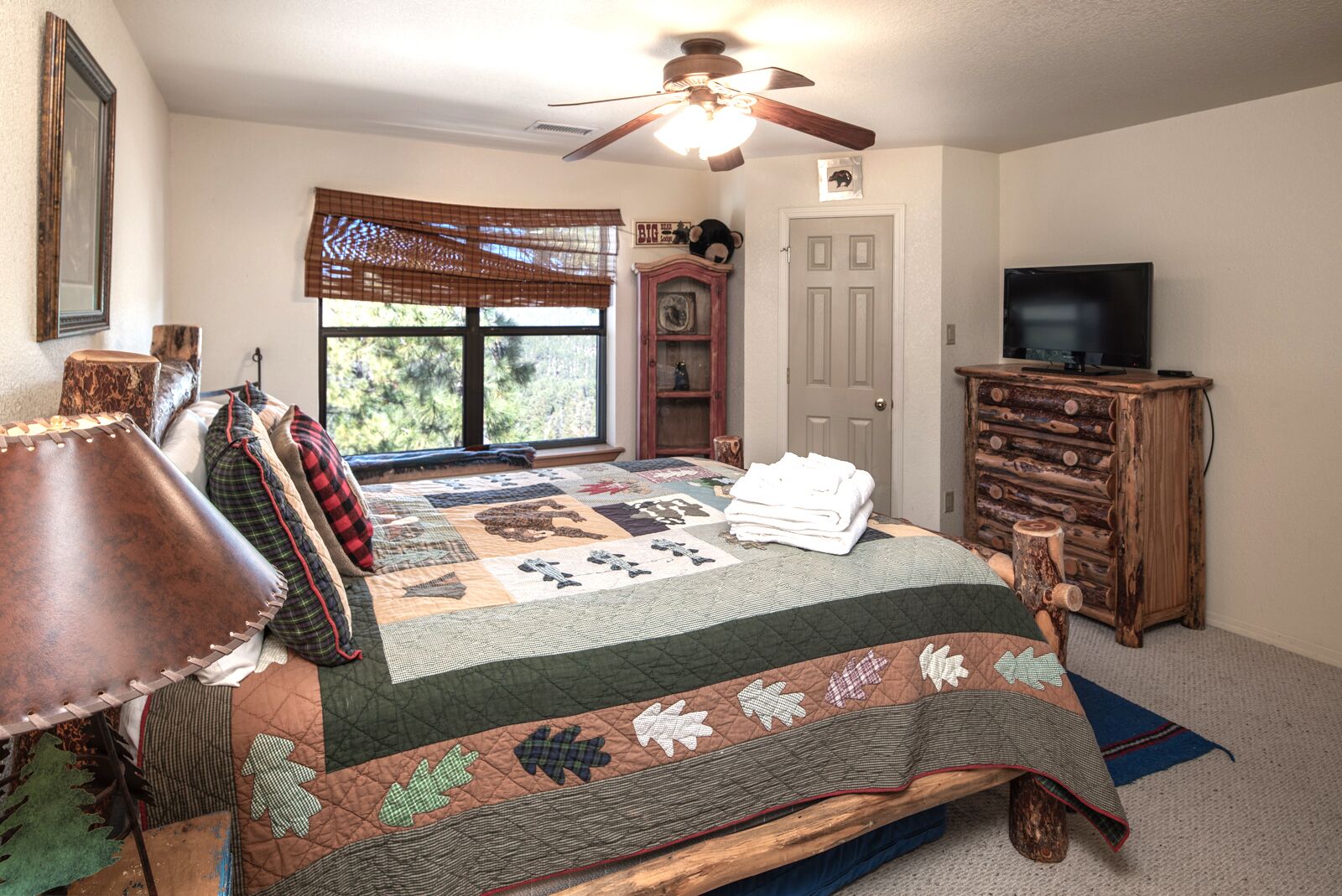 A bedroom with a large bed, a wooden dresser, a television, and a window with blinds.