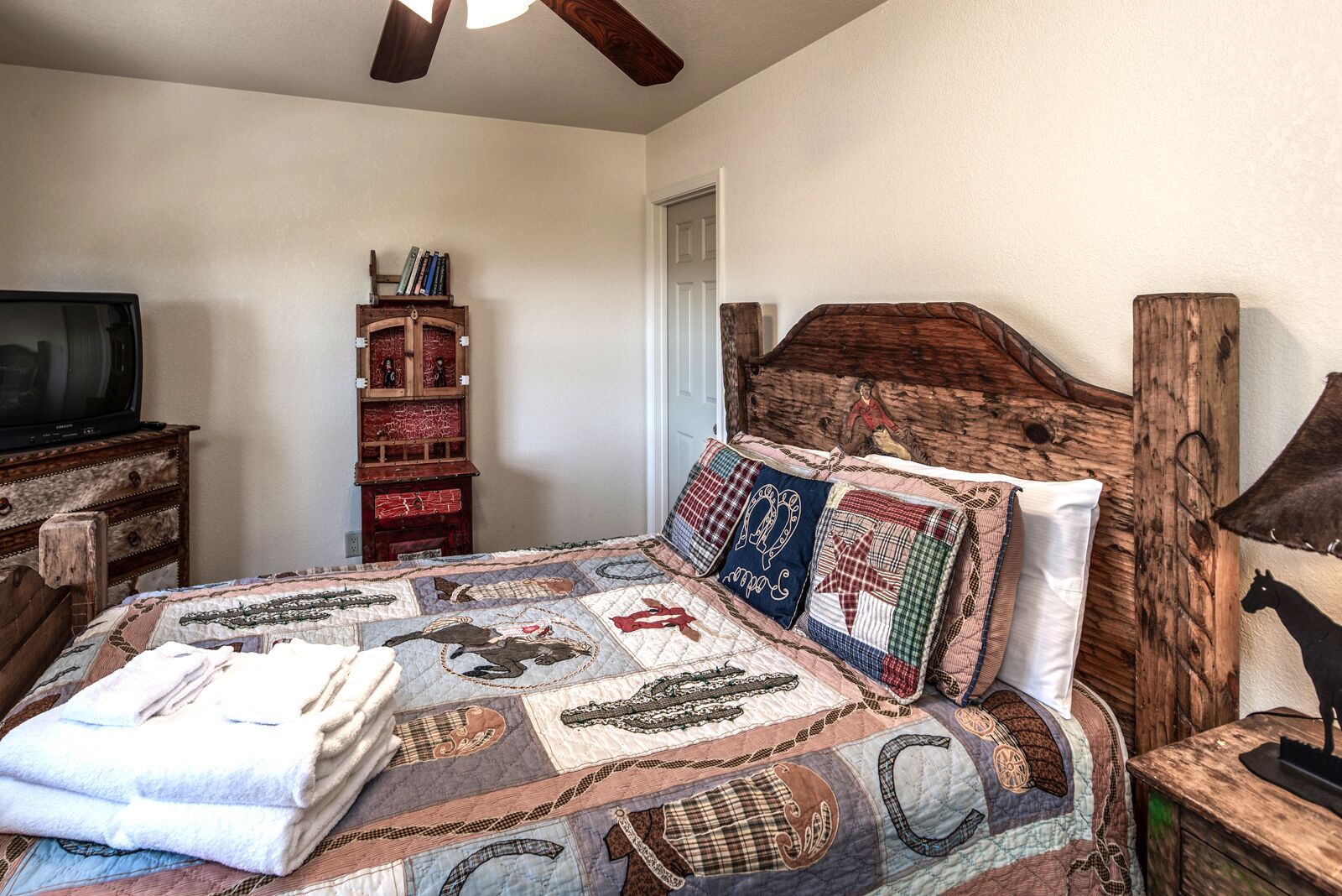 A bedroom with a large bed, a wooden headboard, a wooden dresser, a television, and a wooden cabinet.