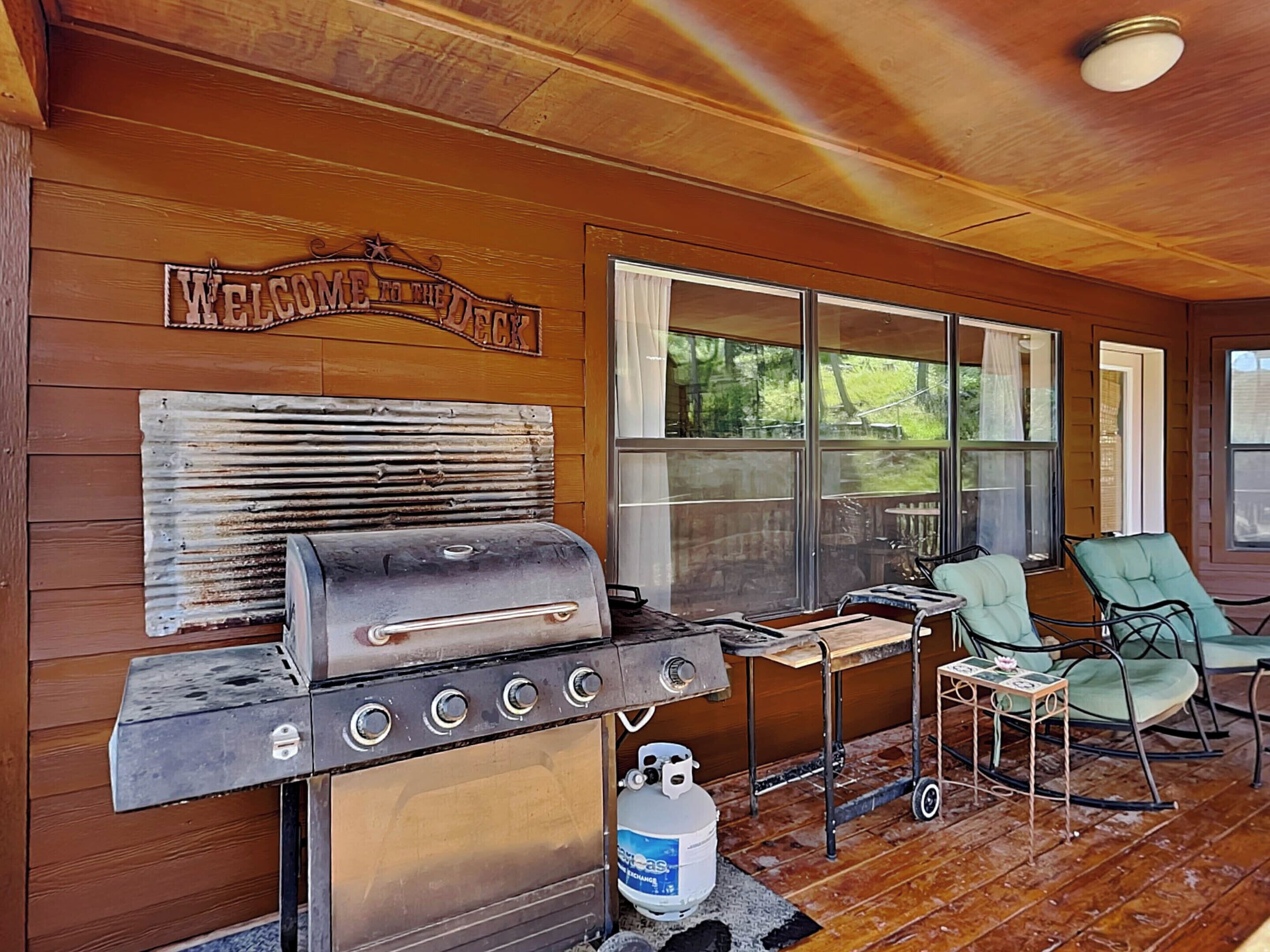 A wooden deck with a grill, outdoor chairs, and a 'Welcome to the Back' sign.