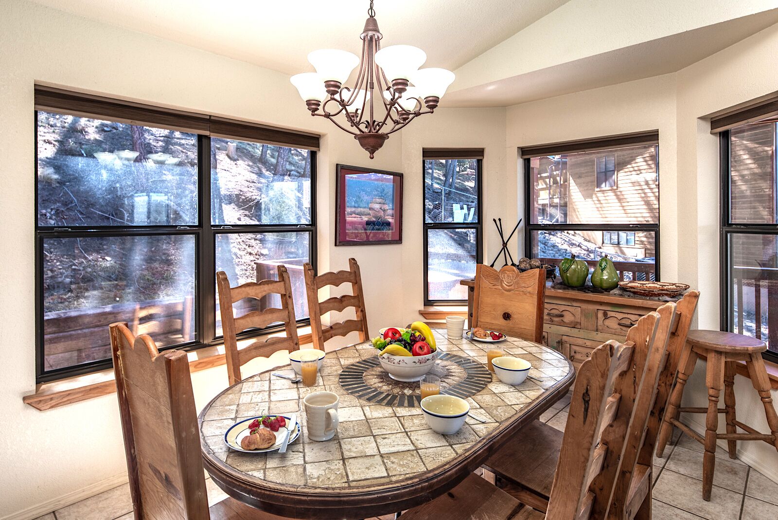 A dining area with a round table, chairs, a chandelier, and large windows with a view of a snowy landscape.