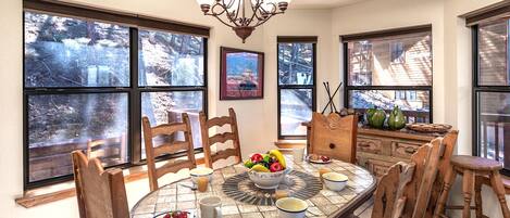 A dining area with a round table, chairs, a chandelier, and large windows with a view of a snowy landscape.