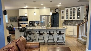 Une cuisine moderne avec des meubles blancs, des appareils en acier inoxydable et un îlot central doté de tabourets de bar.
