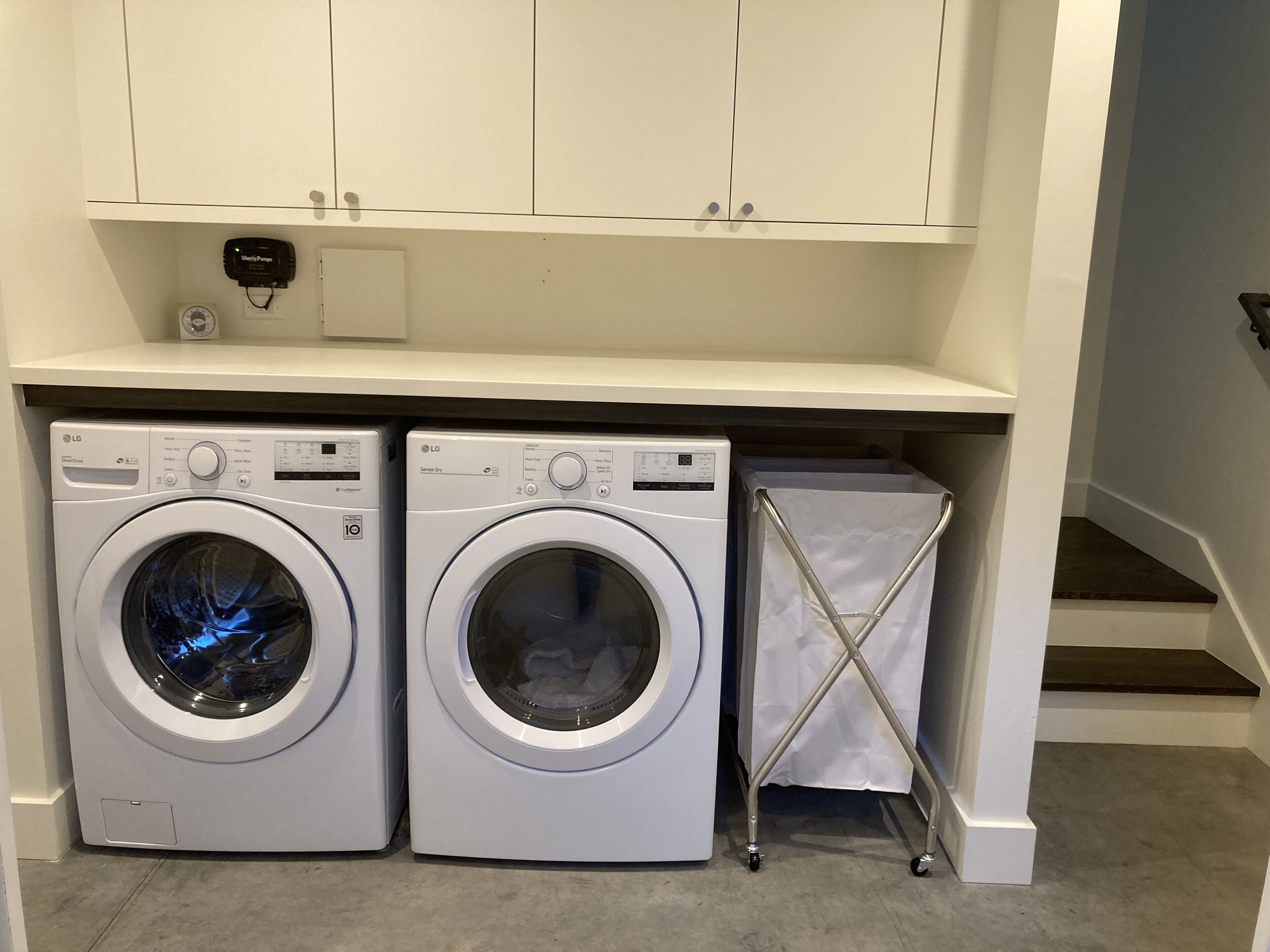 A laundry area with two front-loading washing machines and a drying rack.